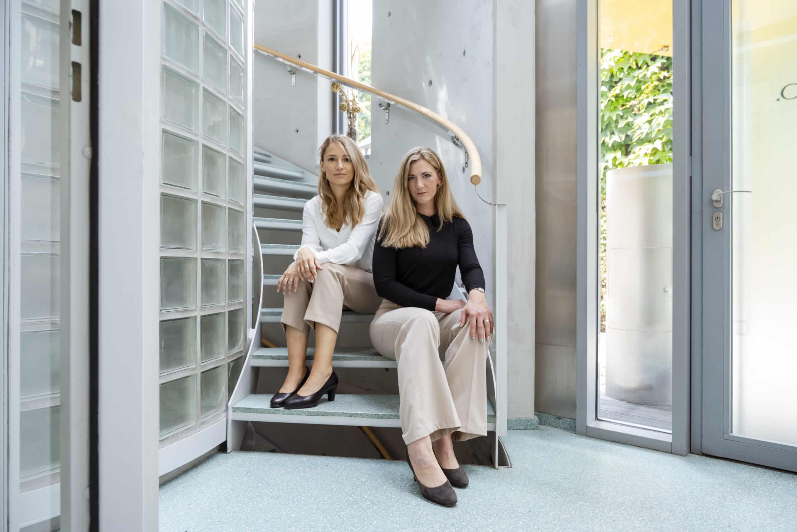 Zwei Mitarbeiterinnen von rt-Hein sitzen auf der Treppe.